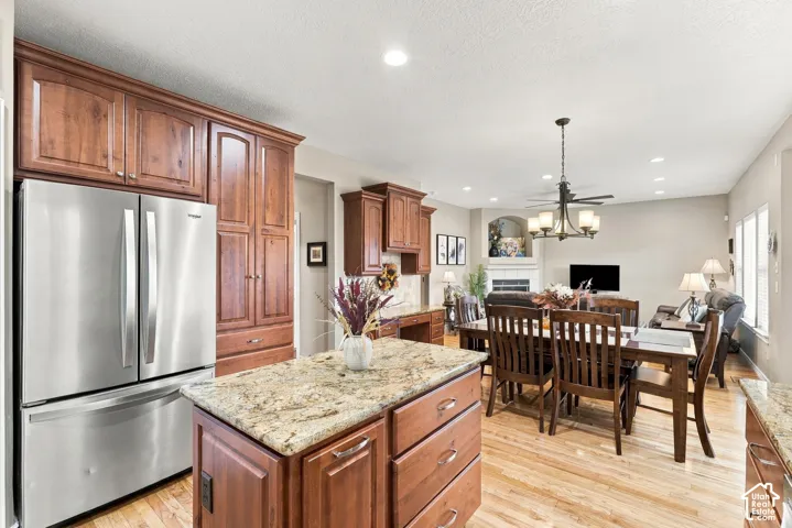 Kitchen featuring stained wood cabinetry, stone countertops, stainless steel French-door refrigerator, integrated island storage, and wood-finish flooring