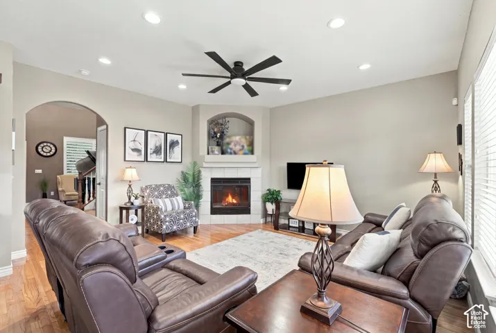 Living room featuring wood-finish flooring, vaulted ceilings with recessed lighting, a ceiling fan, and a tiled fireplace with an arched built-in niche