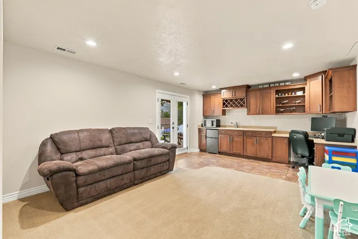 Built-in cabinetry featuring wine storage and display shelving, integrated wet bar with sink, recessed lighting, tile flooring, and double glass doors