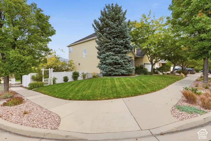 Exterior featuring a corner lot with a manicured lawn, mature trees, white privacy fencing, and an arched gate