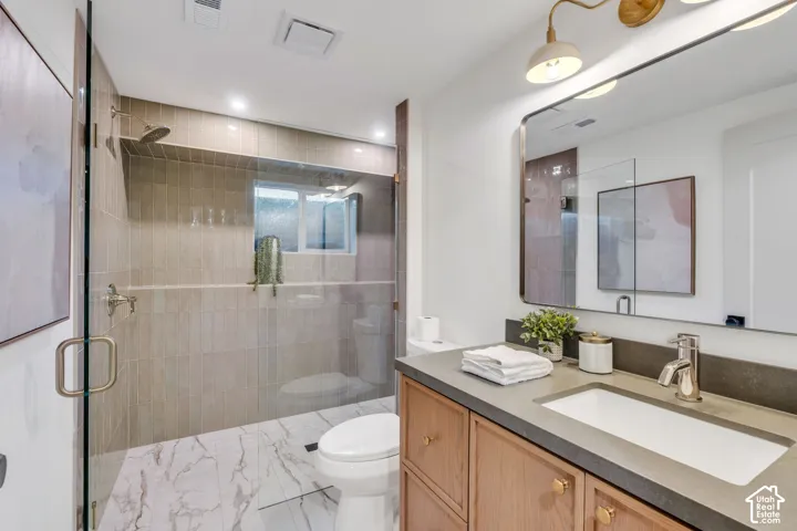 Full-height tiled shower with glass enclosure, custom wood cabinetry, dark countertop with integrated rectangular basin, polished metal hardware, and large-format flooring