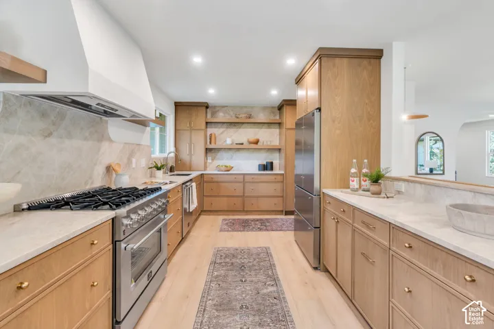 Kitchen featuring light wood-finish cabinetry, stone slab backsplash, quartz countertops, stainless steel professional-style gas range, and wood-finish flooring