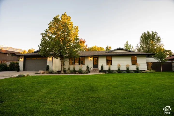 Single-level exterior featuring light-toned horizontal siding, a multi-car garage, large windows with dark frames, and professional landscaping