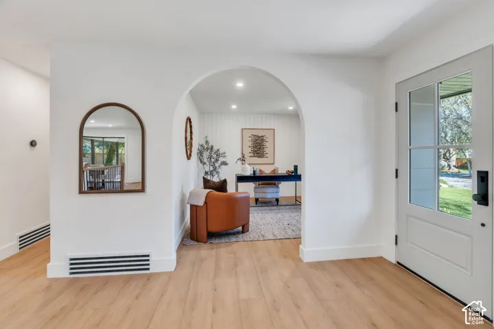 Entryway featuring wood-finish flooring, a glass-paneled entry door, and an arched architectural opening with recessed lighting and vertical wall paneling