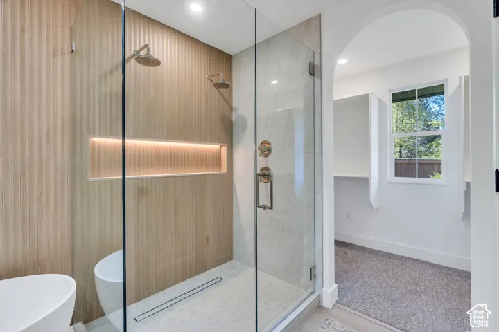 Walk-in shower featuring vertical wood-finish paneling, an integrated wall niche, dual showerheads, stone-textured floor tiling, and a frameless glass enclosure