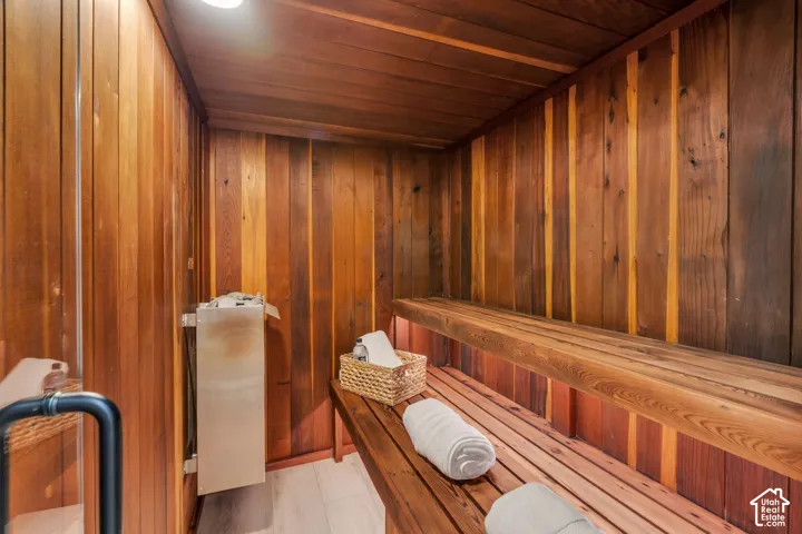Sauna featuring cedar paneling, multi-level wood bench seating, and a mounted metal heating unit