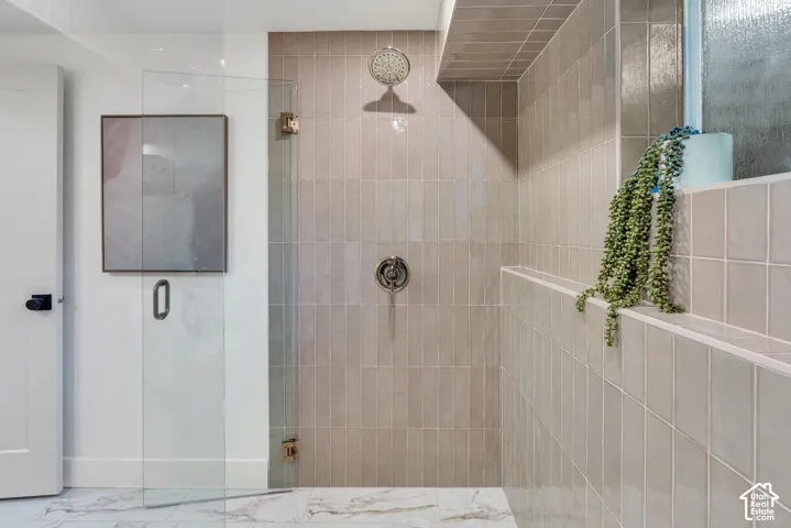 Walk-in shower featuring vertically stacked neutral-toned ceramic tile, glass enclosure, built-in recessed shelving, integrated rainfall showerhead, and stone-finish floor tiling