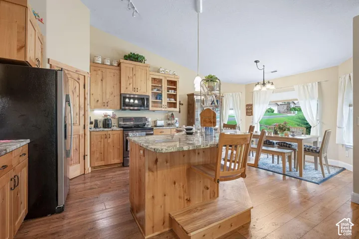 Kitchen featuring wood cabinetry, stone-surface countertops, center island with tiered counter, vaulted ceilings, and wood-finish flooring