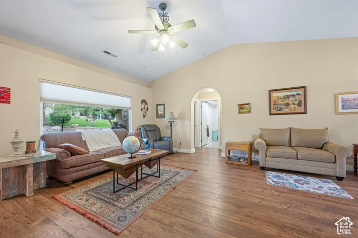 Vaulted ceilings with a central light-integrated ceiling fan, wood-finish flooring, and a large picture window