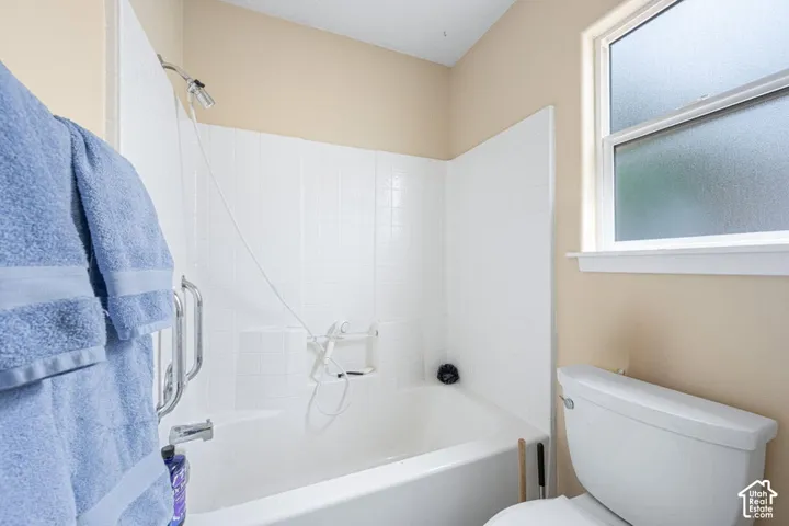 Full-length bathtub with white tiled wall surround, metal grab bar, handheld shower fixture, and frosted glass window