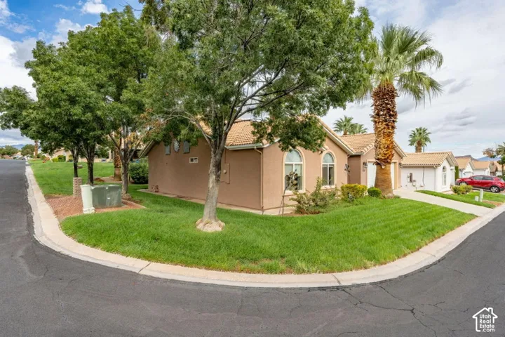 Stucco exterior featuring arched windows, a tile roof, mature landscaping, and a concrete driveway