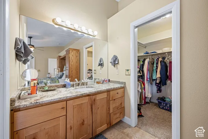 Bathroom vanity with wood cabinetry, stone-finish countertop, undermount sink, full-width mirror, and multi-bulb light fixture