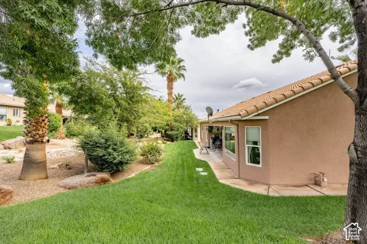 Stucco exterior featuring a tile roof, a manicured lawn, stone hardscaping, and mature palm trees