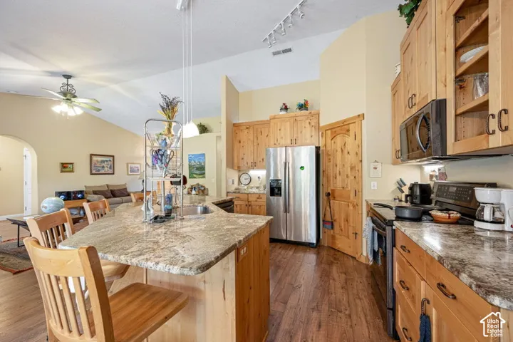Kitchen featuring natural wood cabinetry, stone-finish countertops, stainless steel appliances, wood-finish flooring, and vaulted ceilings