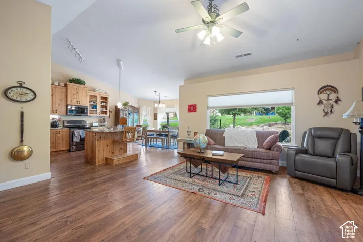 Open-concept interior featuring wood-finish flooring, vaulted ceilings, natural wood cabinetry, a stone-topped kitchen island, and a large picture window