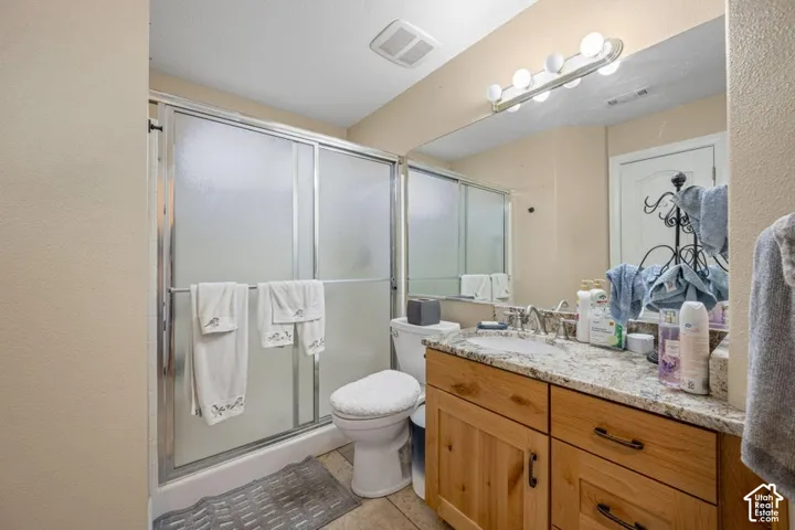 Bathroom featuring a wood vanity with stone-finish countertop, undermount sink, shower with sliding glass doors, and a full-width vanity mirror with integrated lighting