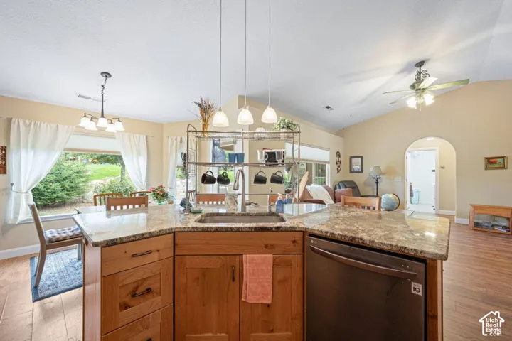 Kitchen island featuring a stone countertop, under-mount stainless steel sink, natural wood cabinetry, built-in dishwasher, and a triple-pendant lighting fixture