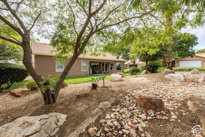 Backyard featuring xeriscaping with decorative rock beds, large landscape boulders, mature trees, and a grass lawn