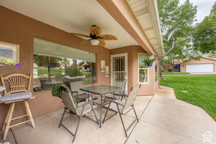 Covered concrete patio featuring a stucco exterior, built-in ceiling fan with leaf-style blades, and large windows