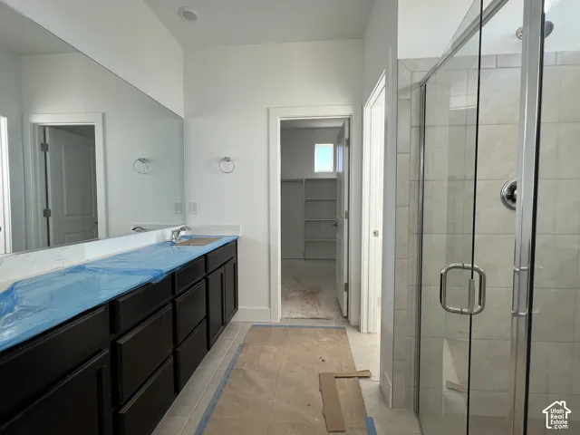 Bathroom featuring dark wood-finish cabinetry, a full-wall mirror, and a glass-enclosed shower with tile surround