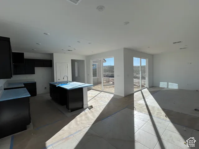 Kitchen featuring dark cabinetry, a central island with a gooseneck faucet, tile flooring, recessed lighting, and sliding glass doors