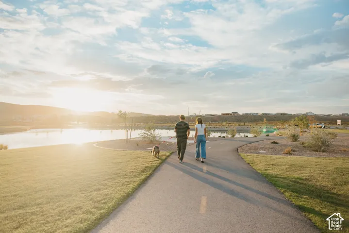Paved community trail surrounded by manicured turf, desert landscaping, and a natural pond backdrop