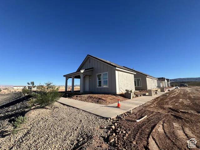 Single-story exterior featuring vertical siding, a covered front porch with timber posts, concrete walkways, and desert landscaping