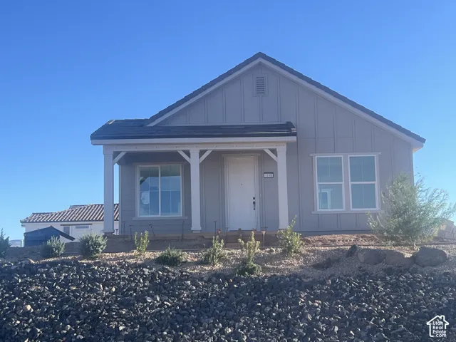 Single-story exterior featuring vertical board-and-batten siding, a covered front porch with decorative brackets, a gabled roofline, and low-maintenance xeriscaped front yard