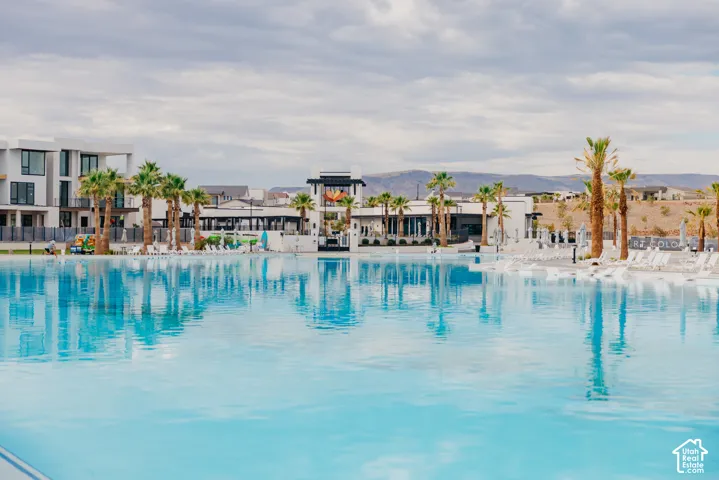 Expansive turquoise swimming pool featuring a beach-entry perimeter, surrounding palm trees, paved pool deck, and mountain backdrop