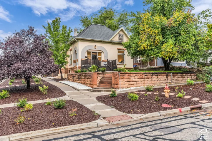 Stucco exterior featuring arched architectural details, sandstone retaining wall, raised front deck, and concrete stairs