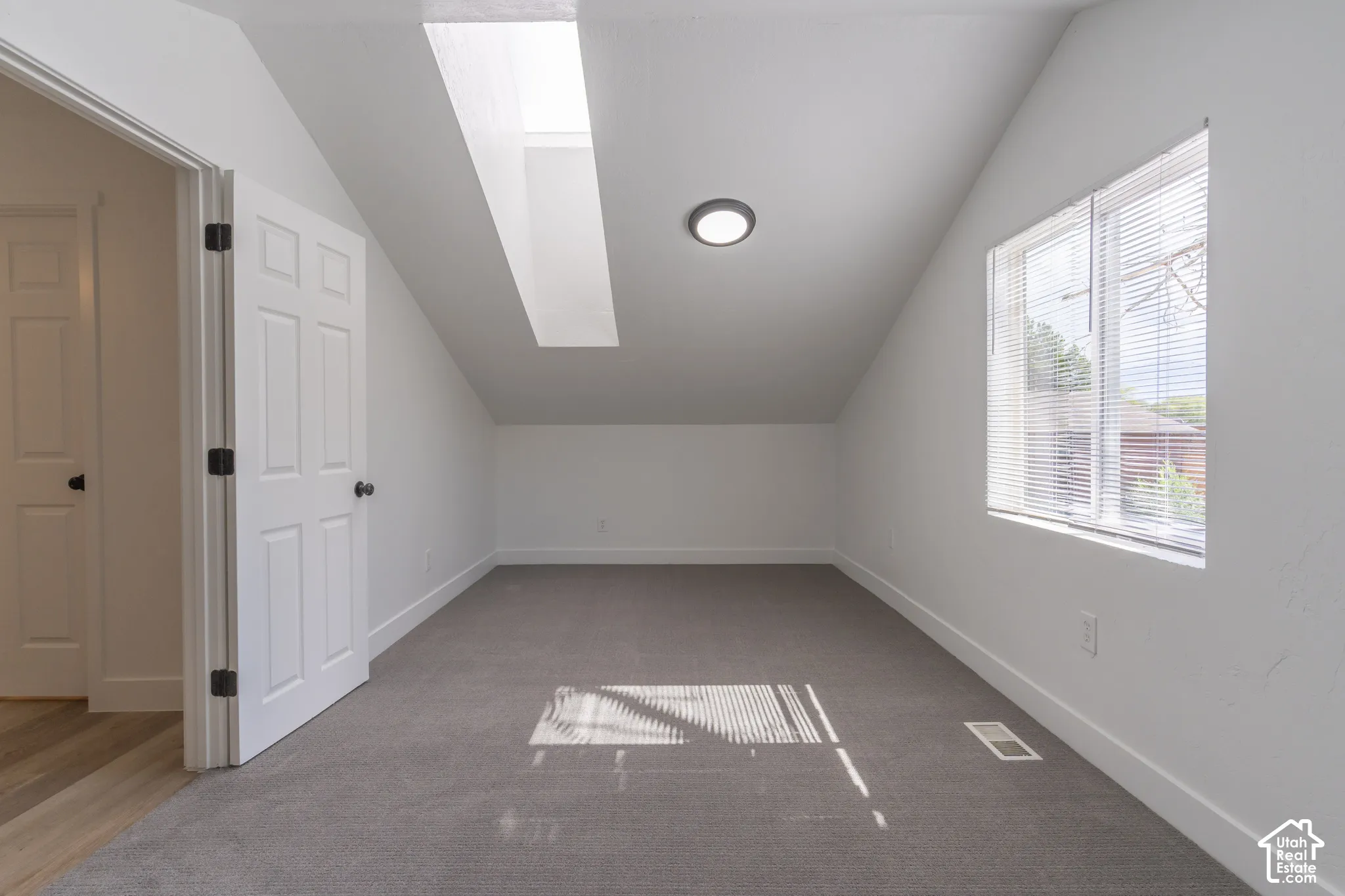 Primary bedroom with vaulted ceilings, a built-in skylight, and new carpet.