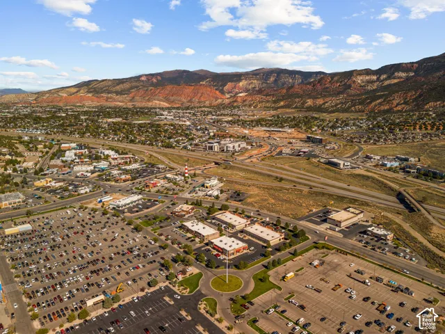Aerial perspective of the surrounding area featuring multi-lane thoroughfares, expansive paved parking surfaces, commercial structures, and a prominent mountain range backdrop