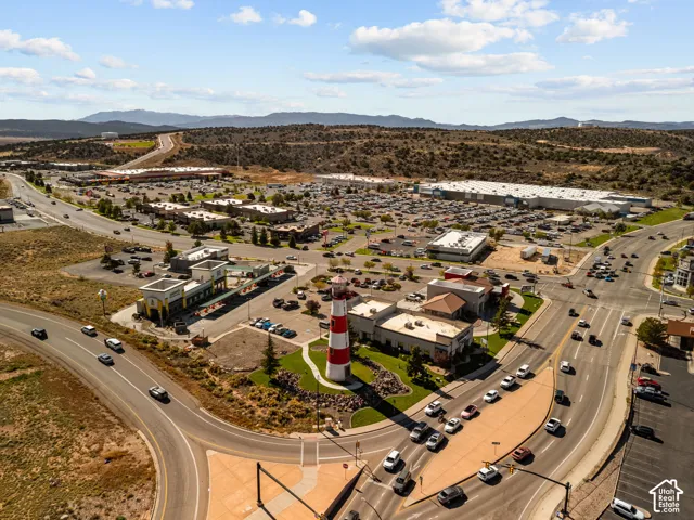 Aerial perspective of a commercial site featuring a red-and-white striped lighthouse structure, paved parking areas, curated landscaping with stone accents, and road infrastructure