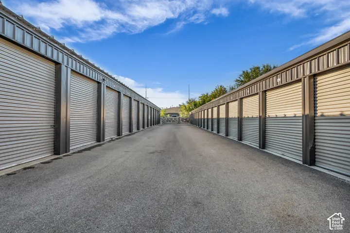 Storage facility featuring metal-sided individual units, roll-up doors, paved driving lane, and secure perimeter fencing