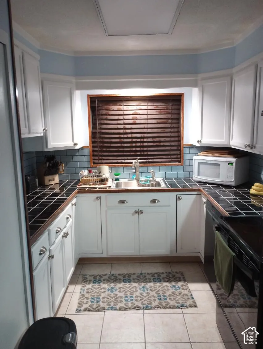 Kitchen featuring white cabinetry, black square-tile countertops, a light blue subway-tile backsplash, and a stainless steel dual-basin sink with a goose-neck faucet
