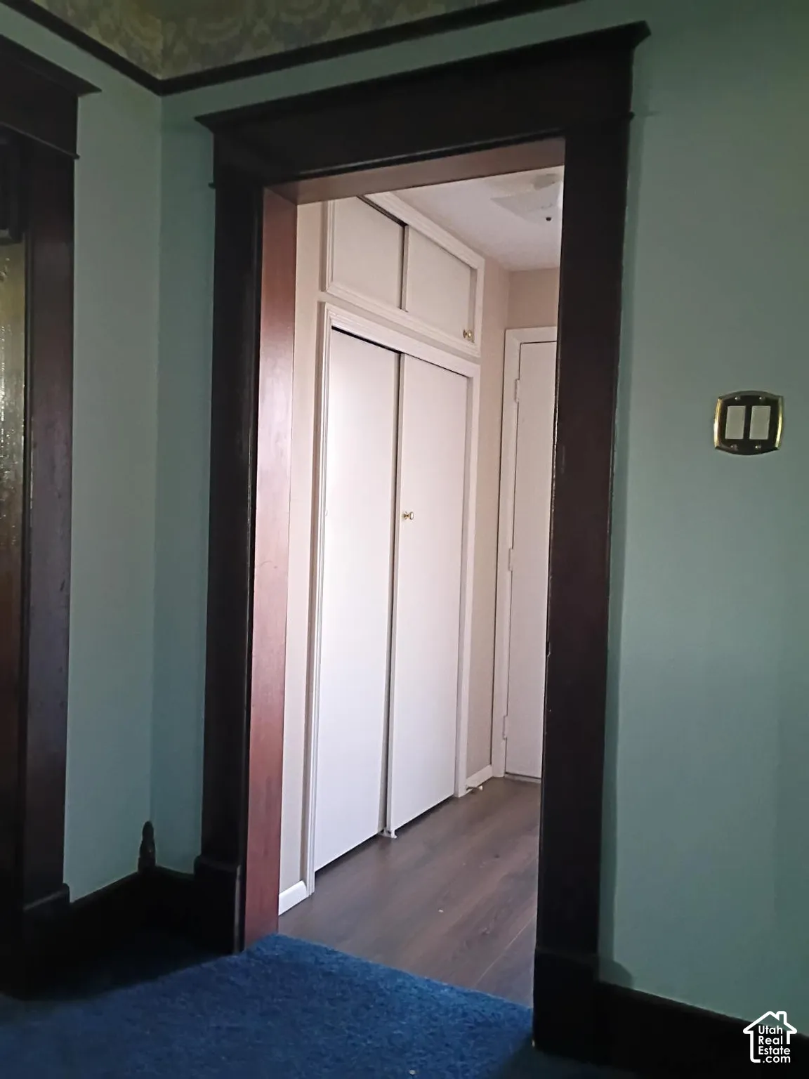Original dark wood door casing featuring architectural crown headers, wood-finish flooring, and built-in closet storage with overhead cabinetry