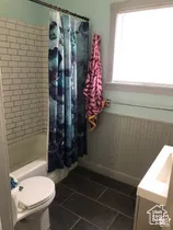 Bathroom featuring subway tile shower surround, beadboard wainscoting, large-format tile flooring, and a window with wood casing