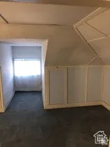 Attic space featuring slanted ceilings, paneled walls, a recessed window alcove, and carpeted flooring