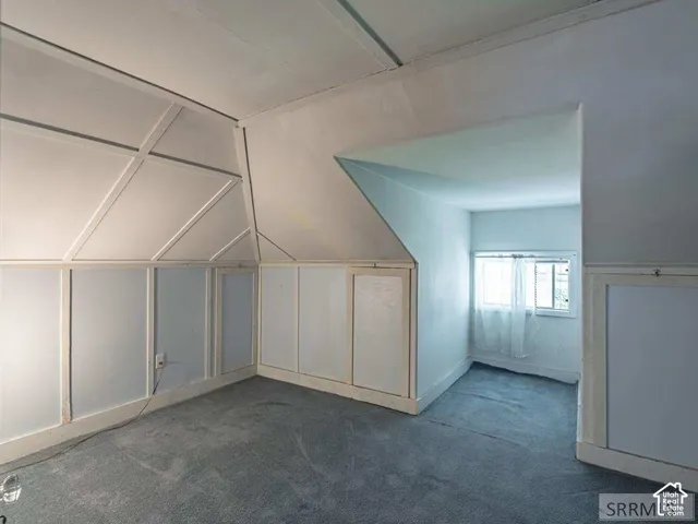 Attic space featuring slanted walls, decorative wood paneling, built-in access doors, and a window with natural light