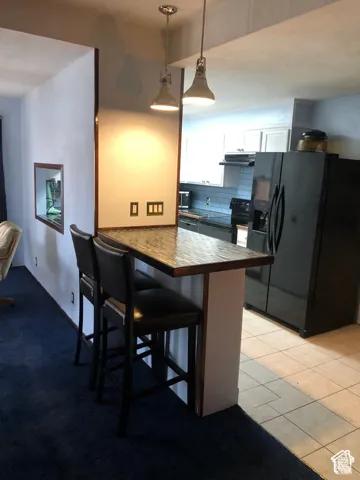 Kitchen breakfast bar featuring a textured surface, dual industrial-style pendant lighting, ceramic tile flooring, and integrated kitchen cabinetry