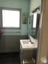 Bathroom featuring a vanity with an integrated rectangular sink, gray beadboard wainscoting, dark tile flooring, a mirrored medicine cabinet, and a multi-light fixture