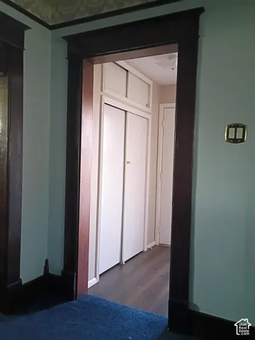 Original dark wood door casing featuring architectural crown headers, wood-finish flooring, and built-in closet storage with overhead cabinetry