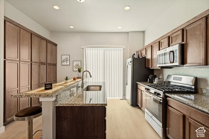 Kitchen featuring wood cabinetry, stone countertops, an island with an integrated sink, stainless steel appliances, and wood-finish flooring