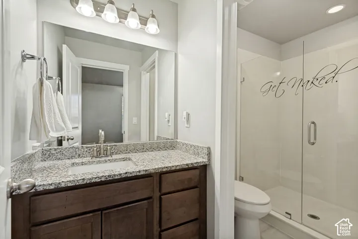 Bathroom featuring dark wood-finish cabinetry, stone-surface countertop with an undermount sink, multi-bulb vanity lighting, and a glass-enclosed shower with a polished chrome handle