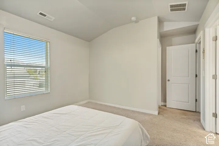 Neutral-toned room featuring a vaulted ceiling, wall-to-wall carpeting, and a single-pane window with horizontal blinds