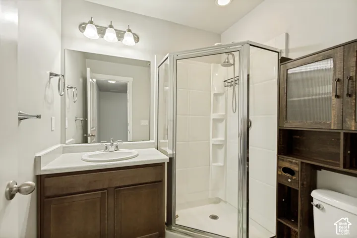 Bathroom featuring a dark wood vanity with a light-toned countertop, integrated oval sink, chrome-finished shower enclosure with built-in shelving, and attached dark wood cabinetry