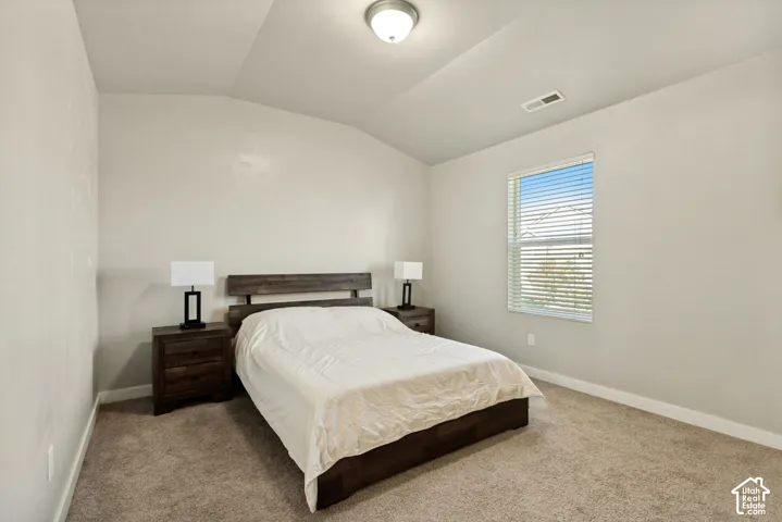 Neutral-toned interior featuring a vaulted ceiling, wall-to-wall carpeting, and a window with integrated blinds