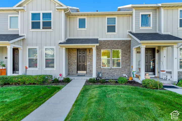 Multi-story residence featuring light gray vertical siding, stone veneer accents, dark-toned front entry doors, and a concrete walkway