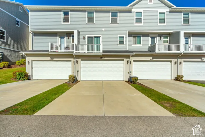 Multi-level townhome exterior featuring horizontal siding, private attached garages, concrete driveways, and upper-level balconies with white railings