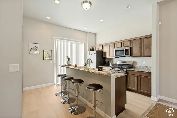 Kitchen featuring wood cabinetry, stone-finish countertops, stainless steel appliances, breakfast bar, and wood-finish flooring